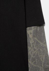 Manche courte noire superposée à une manche longue grise avec un subtil motif floral abstrait sur tissu tricoté.