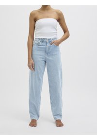 Světlé modré džíny s vysokým pasem, volného střihu a pěti kapsami. Nošené s bílým topem bez ramínek, outfit má minimalistický design.