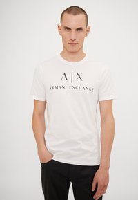 Hvit bomull T-skjorte med rund hals, korte ermer og mørk trykk av "A|X ARMANI EXCHANGE" på forsiden.
