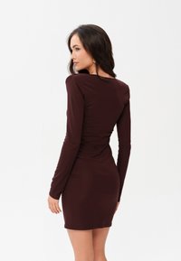 Dopasowana sukienka z długim rękawem w głębokim burgundzie. Miękki, elastyczny materiał o gładkiej teksturze. Długość do połowy uda z okrągłym dekoltem.
