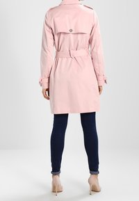 Jasnoróżowy płaszcz trencz z paskiem w talii, zapinanymi na guziki pagonami na ramionach oraz rozcięciem z tyłu. Noszony na ciemnoniebieskich obcisłych dżinsach i beżowych szpilkach.