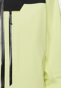 Helle gelbe wasserdichte Jacke mit einer schwarzen Reißverschlusstasche, strukturierten schwarzen Akzenten und einem schlanken, modernen Design.
