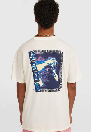 Camiseta oversize de color crema que presenta un gráfico vibrante en la parte posterior con tonos azules y morados, enmarcado por un borde decorativo.