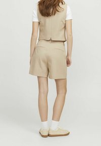 Beige vest and matching shorts, crafted from a textured fabric, featuring a tailored fit, back pockets, and a clean, minimalist design.