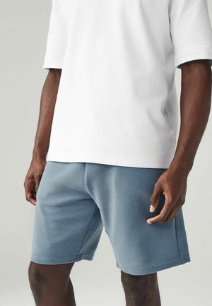 Hellgraues T-Shirt mit kurzen Ärmeln und rundem Halsausschnitt, kombiniert mit strukturierten blauen Shorts. Die Shorts verfügen über horizontale Streifendetails und seitliche Taschen.