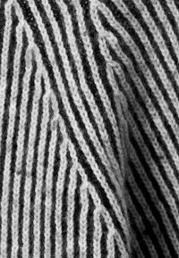 Gros plan d'un tissu tricoté noir et blanc avec un motif à rayures diagonales et une texture visible des fibres de fil.