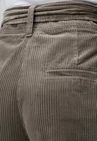 Gros plan sur un pantalon en velours côtelé beige montrant des rainures verticales, une passants de ceinture et une poche arrière avec des coutures détaillées.