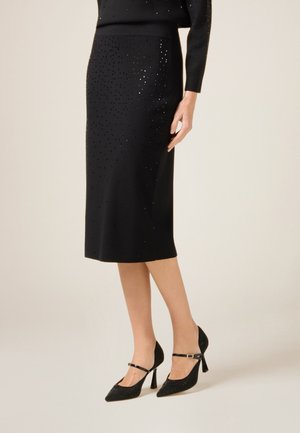Sort strikking blyantskirt med tekstureret overflade, der har spredte perler. Sæt sammen med spidse sorte hæle med ankelrem.