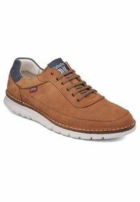 Zapatilla de ante marrón con suela de goma blanca, que cuenta con un talón de ante azul marino, cierre de cordones y costuras decorativas a lo largo de los lados.