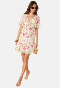 Robe florale avec un décolleté en V profond, manches courtes à volants, dans des couleurs pastel. Un tissu léger avec des fleurs roses sur un fond crème.