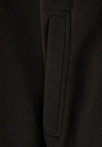 Svart fleece-stoff med design for frontlomme. Myk tekstur med en jevn overflate og minimale sømmer for en ren finish.