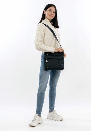 Black crossbody bag made of textured fabric, featuring two zippered pockets and a detachable strap. Smooth hardware accents enhance the design.