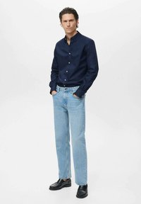 Camicia azzurra con bottoni, jeans dritti blu chiaro, scarpe nere. La camicia presenta un colletto e chiusura con bottoni. I jeans hanno un design classico a cinque tasche.