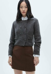 Cardigan grigio in lana con colletto, design doppiopetto, finitura testurizzata e tasche frontali, indossato sopra una gonna marrone.