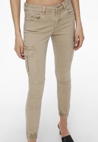 Beige cargobyxor med slim fit, som har flera fickor, elastiska ärmslut och ett slätt, lätt tyg.