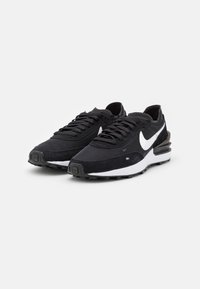Scarpe Nike in bianco e nero caratterizzate da un mix di materiali lisci e testurizzati, lacci prominenti e un design distintivo della suola curvata.