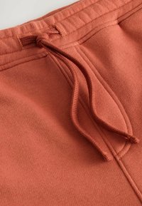 Rustfarvede sweatpants med tekstureret stof, der har en snoretræk i taljen og sidelommer, samt syningdetaljer.