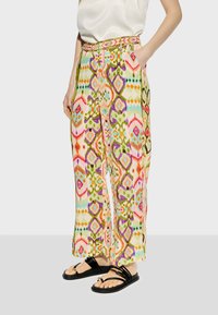 Färgglada, mönstrade vida byxor med dragsko i midjan, prydda med rosa, gröna och blå geometriska mönster. Bärs med svarta sandaletter med remmar.