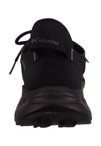Zwarte sportieve schoen met een gestructureerde zool, elastische veters en Columbia-logo op de hiel. Beschikt over ademend materiaal en een ondersteunend ontwerp.