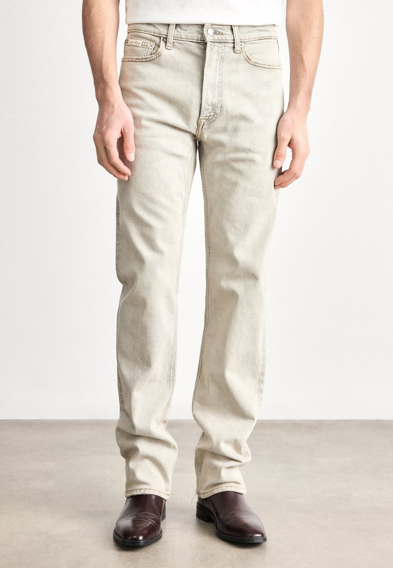 Gaiši bēšas džinsa bikses ar taisnu piegriezumu, ar priekšējām kabatām, pogas aizdari un redzamu šuvju izšuvumu. Kombinētas ar tumši brūnām zābakiem.