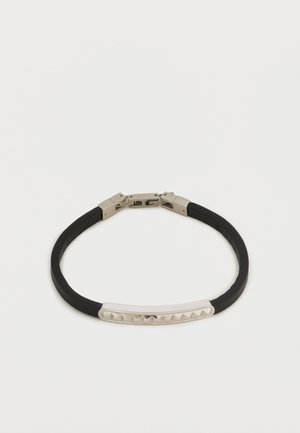 Czarna gumowa bransoletka z srebrną zapinką i zakrzywioną srebrną płytką z małymi piramidalnymi ćwiekami na środku.