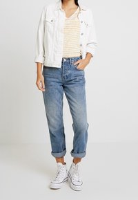 Chaqueta de mezclilla blanca, camiseta de rayas amarillas y blancas, jeans azules doblados, zapatillas altas blancas. Outfit casual con texturas superpuestas.