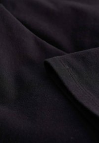 Fekete szövet, sima textúrával és enyhe fényléssel. Hajtott széllel, diszkrét varrással és árnyékokkal, amelyek mélységet adnak a szövetnek.