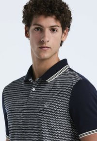 Polo bleu marine en tissu à motif texturé, avec des manches unies contrastées, une patte de boutonnage à deux boutons et un col à côtes avec des rayures blanches.