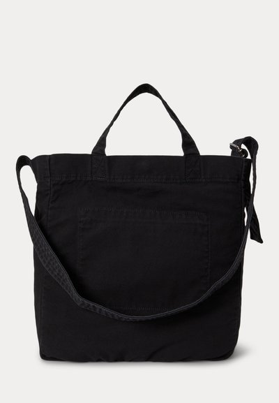 Czarna torba materiałowa w kształcie kwadratu z krótkimi uchwytami, długim regulowanym paskiem na ramię oraz przednią naszywką z kieszenią.