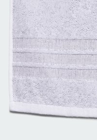 Biała bawełniana ręcznik o teksturowanej powierzchni, z trzema poziomymi tkanymi pasami. Miękki, chłonny materiał z gładką krawędzią.