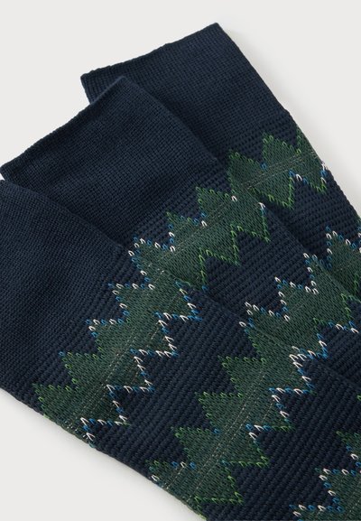 Chaussettes tricotées bleu foncé avec un motif en zigzag vert bordé de points blancs et bleus, posées à plat sur un fond blanc.