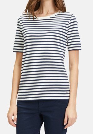 Femme portant un t-shirt à manches courtes à rayures horizontales blanches et bleu marine avec un pantalon bleu marine, cadrée du cou aux hanches.
