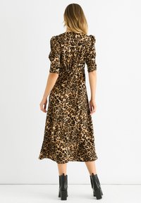 Kleid mit Leopardenmuster aus weichem Stoff, in midi Länge, mit Puffärmeln und tailliertem Schnitt, kombiniert mit klobigen schwarzen Stiefeln mit Absatz.