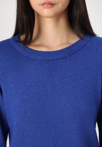 Pull bleu en maille avec un col rond côtelé et une texture lisse. Coupé jusqu'à la poitrine, avec des manches longues ajustées.