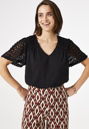 Black top with lace short sleeves and a V-neck. Paired with patterned pants featuring red, cream, and black diamond shapes. Elegant texture.