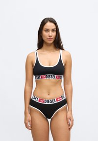 Conjunto de soutien desportivo e biquíni preto com acabamento branco. O soutien apresenta uma faixa central com o logótipo DIESEL em vermelho e branco, com o logótipo correspondente na cintura do biquíni.