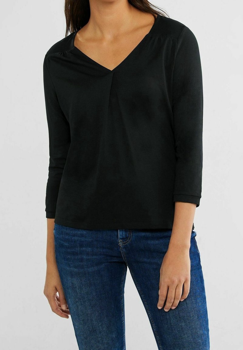 Svart topp med trekvartsärmar och V-ringning. Tillverkad av mjukt material, med diskret rynkning vid axlarna och en avslappnad passform.