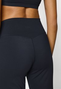 Hoge taille zwarte leggings gemaakt van rekbare stof, met een gladde textuur, minimale naden en subtiele branding nabij de tailleband.