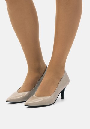 Scarpe con tacchi alti in pelle sintetica beige, con punta affilata, scollatura bassa e un sottile tacco nero, che mostrano una finitura liscia e lucida.