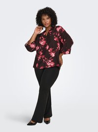 Black blouse with pink floral pattern, v-neckline, and ¾ sleeves. Paired with black slacks and pointed-toe shoes, showcasing a relaxed fit.