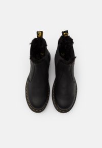 Botas de cuero negras hasta el tobillo con interior aterciopelado, costuras amarillas, paneles laterales elásticos y una lengüeta de tirón con texto.