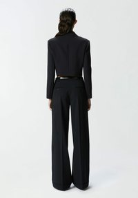 Skraćeni crni sako s ogrlicom, uparen s hlačama visokog struka i širokim nogavicama. Krojen dizajn i glatka tekstura tkanine.