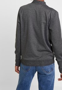 Grijze pullover sweatshirt met een hoge kraag, textuurstof, ribbelboorden en -zoom, gecombineerd met blauwe spijkerbroek. Eenvoudig ontwerp, geen patronen.