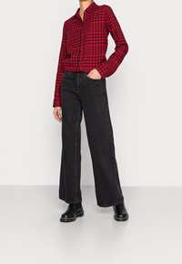 Red and black plaid button-up shirt paired with high-waisted, black wide-leg jeans. Boots feature a chunky sole and stitched detailing.