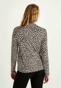 Haut à manches longues en tissu léger, présentant une base beige avec un imprimé léopard noir et marron, coupe ajustée, ourlet arrondi et col standard.