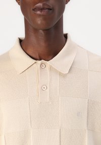Beige kötött polo ing kockás mintával, gallérral és két gombos nyakkal, strukturált anyagból, kis logóval.
