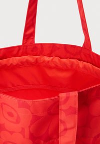 Κόκκινη τσάντα tote με ανθικό σχέδιο, ανοιχτό πάνω μέρος και μακριές υφασμάτινες λαβές, φαίνεται από πάνω.