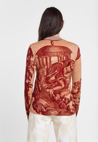 Haut à manches longues avec un motif graphique de style baroque rouge et orange, finition texturée et col rond. Motif et détails subtils sur le tissu.