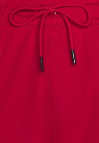 Röda badbyxor med dragsko i midjan med svarta spetsar, slät textur och minimal sömnadsdetalj.