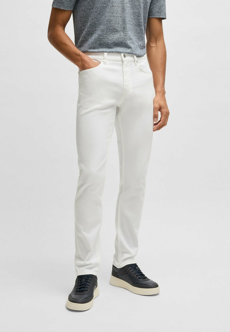 Białe jeansy o dopasowanym kroju, pięć kieszeni i zapięcie na guzik. Połączone z czarnymi trampkami i szarym t-shirtem.